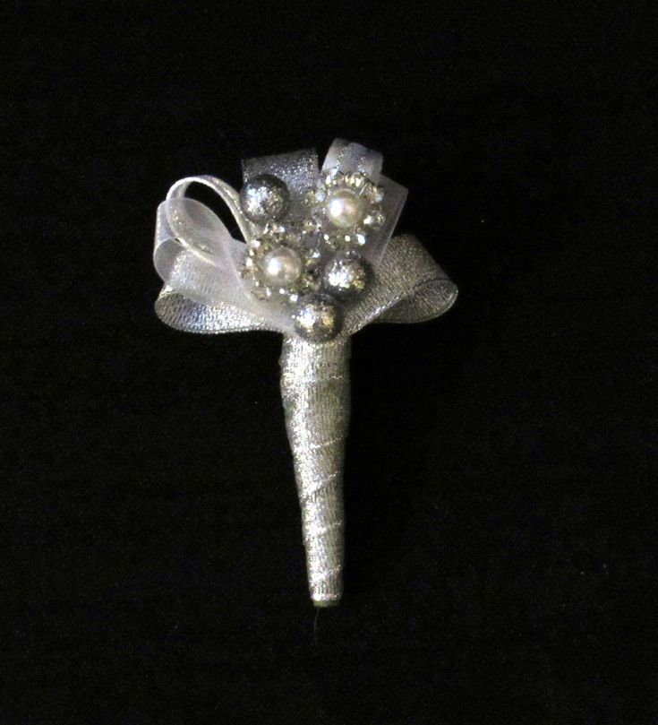 a silver boutonniere with pearls and bows on black background, closeup