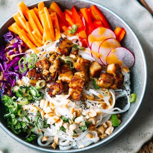 a bowl filled with noodles, carrots, and other veggies next to chopsticks