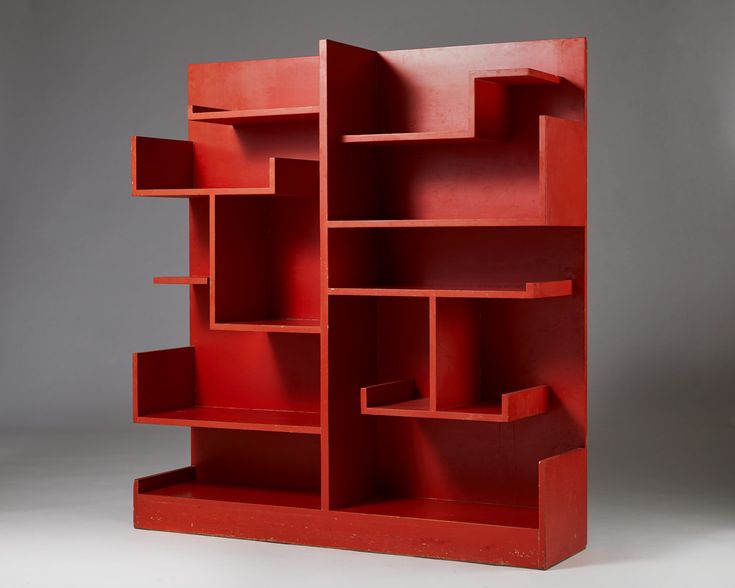 a red book shelf sitting on top of a white floor next to a gray wall