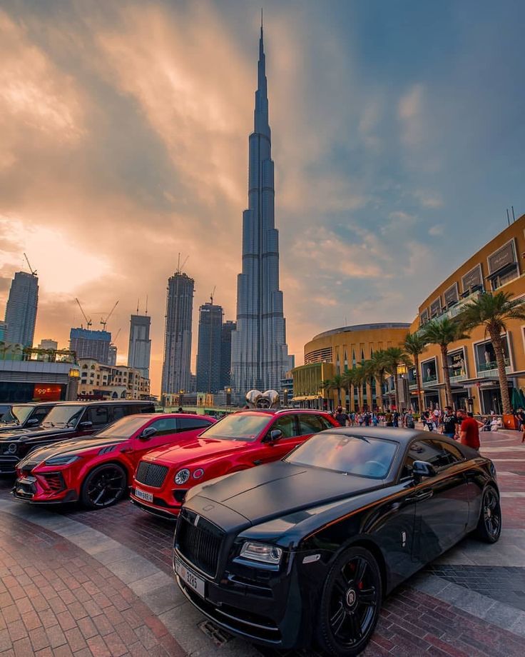 several luxury cars parked in front of the burj dubai skyline at sunset or dawn