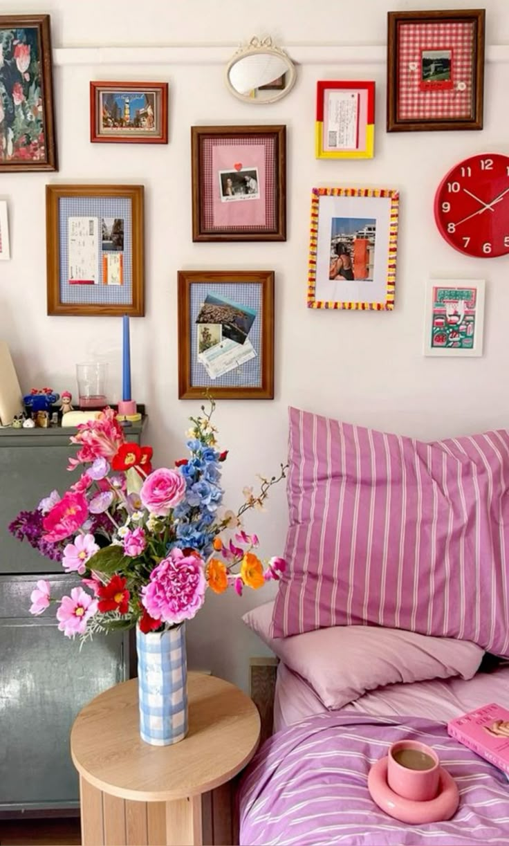 a bedroom with pink and white bedding, pictures on the wall and flowers in a vase