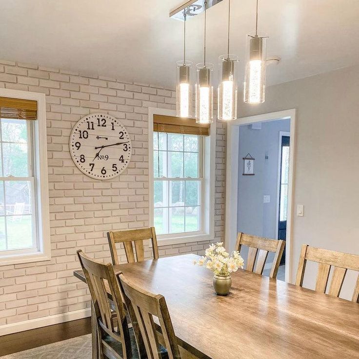 a dining room table and chairs with a clock on the wall behind it in front of two windows