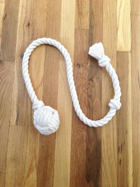 a white rope with a knot on it laying on a wooden floor next to a ball of yarn