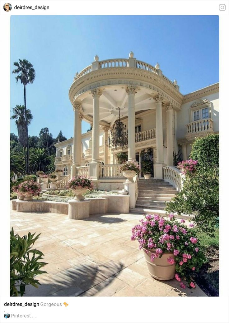 a large white house with lots of flowers in the front yard and stairs leading up to it