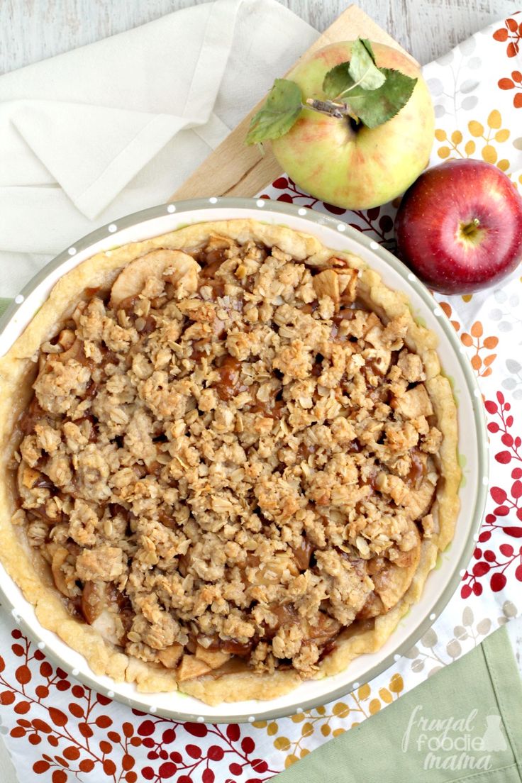 an apple pie sitting on top of a table next to two apples and a napkin