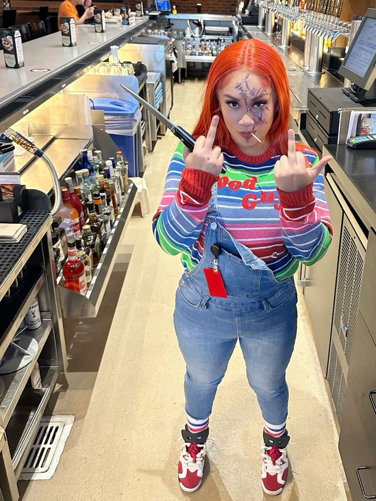 a woman with red hair and makeup making the peace sign while standing in a kitchen