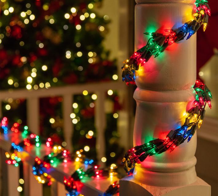 a christmas tree is lit up with lights on the outside of it and in the background, a white picket fence