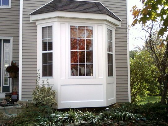 a small white window on the side of a gray house in front of a tree