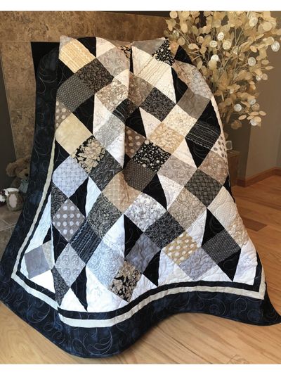 a black and white quilt sitting on top of a wooden floor next to a vase with flowers