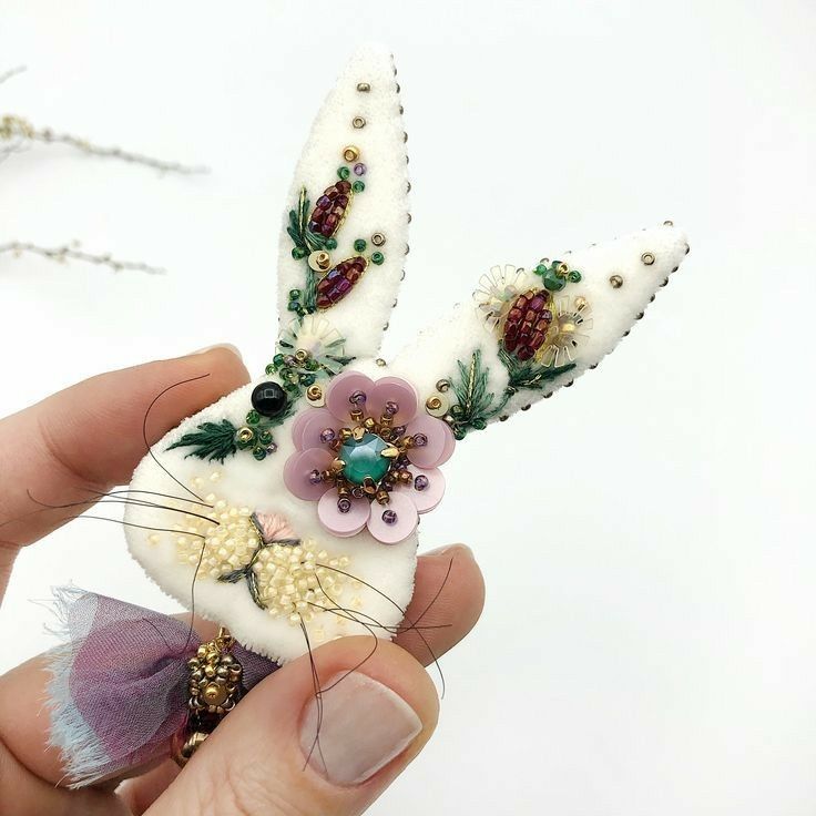 a hand holding a small white rabbit with flowers on it's ears and tail