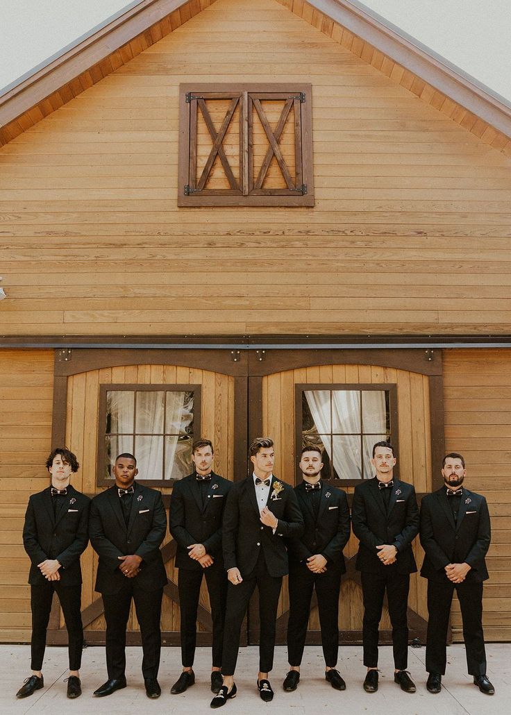 a group of men standing next to each other in front of a wooden building with doors