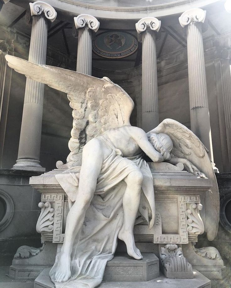 an angel statue sitting on top of a bench in front of some tall pillars and columns