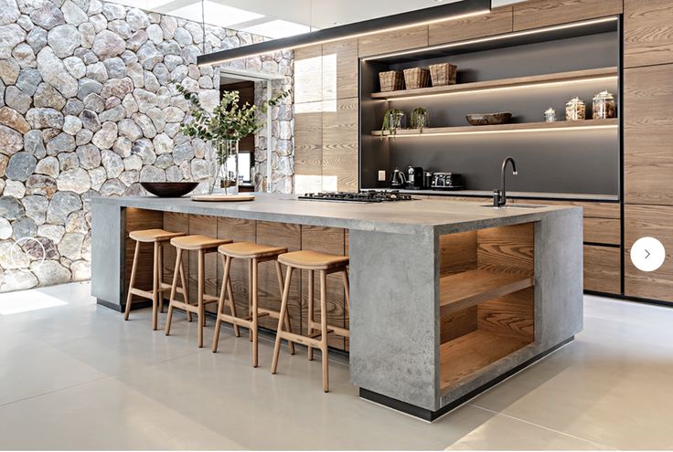 a kitchen island with stools in front of it next to a stone wall and shelves