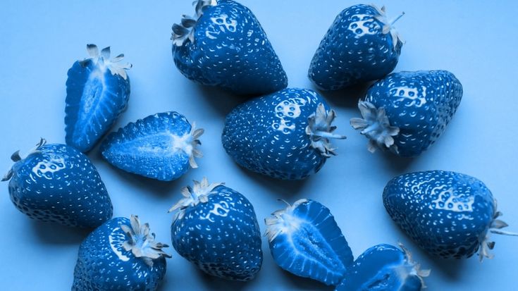 blue strawberries are arranged on a light blue surface with white flowers and letters painted on them