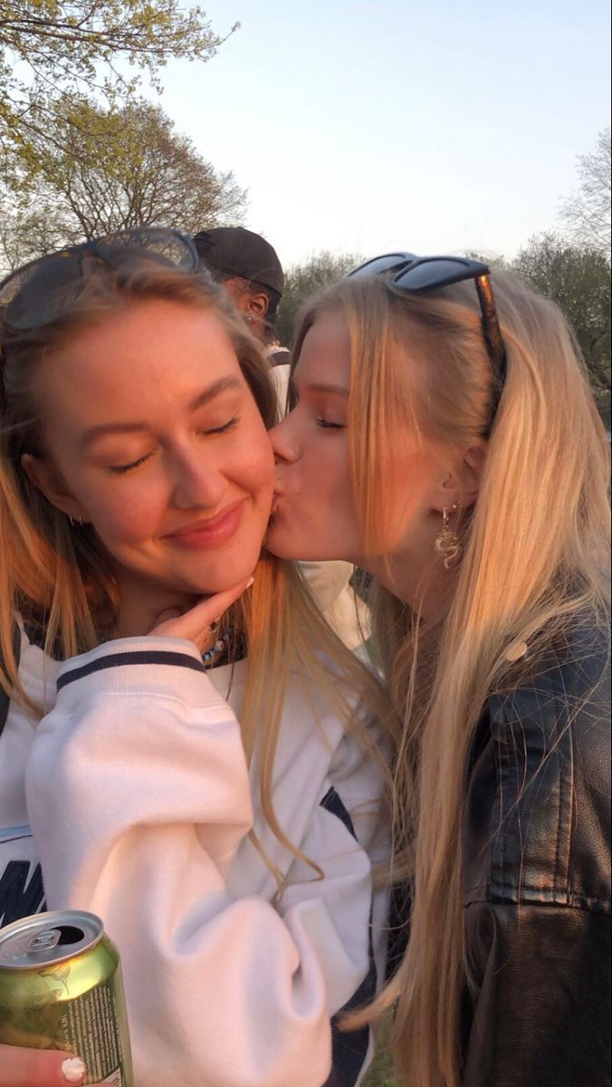 two young women kissing each other while holding cans