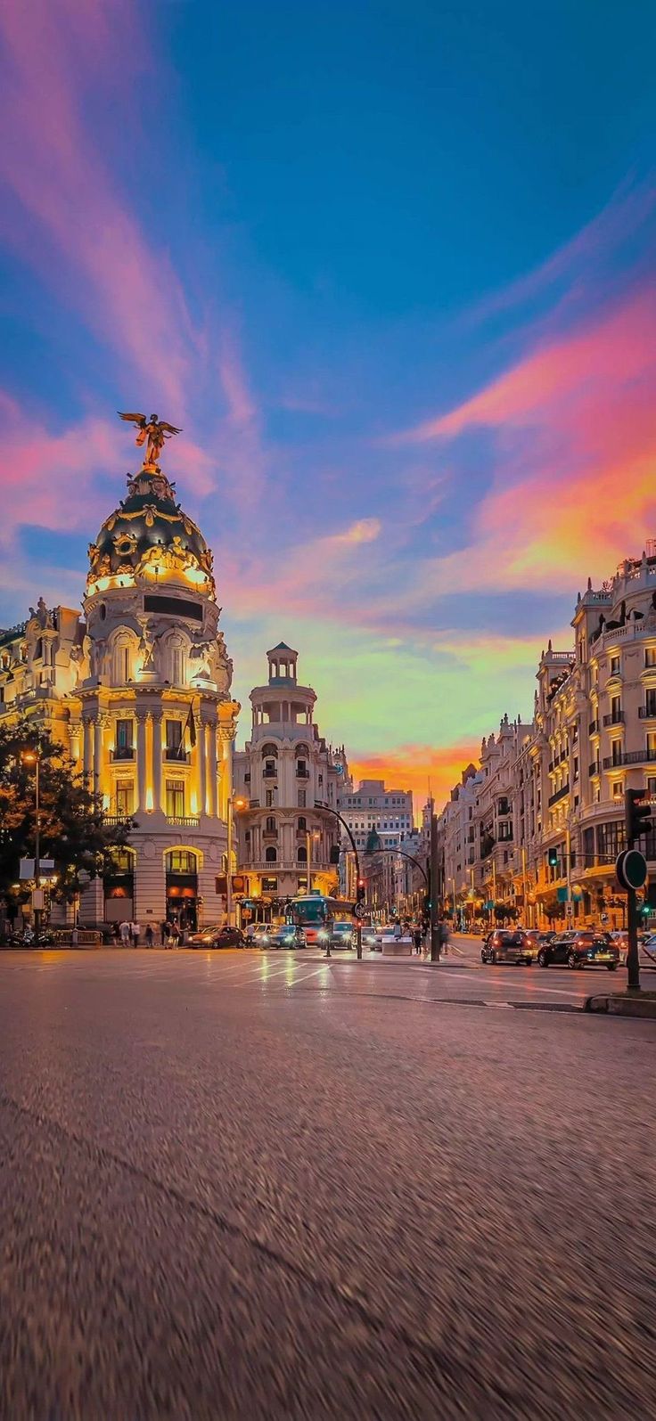 an empty city street at dusk with the sun setting in the background and buildings lit up