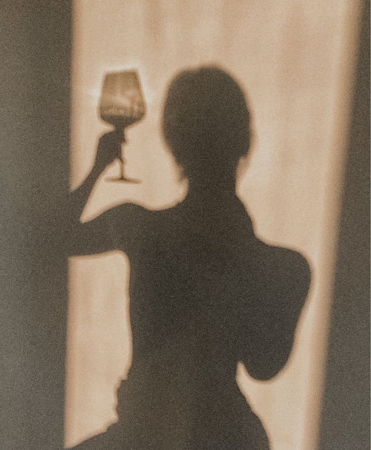 the shadow of a woman holding a wine glass in front of her face and arm