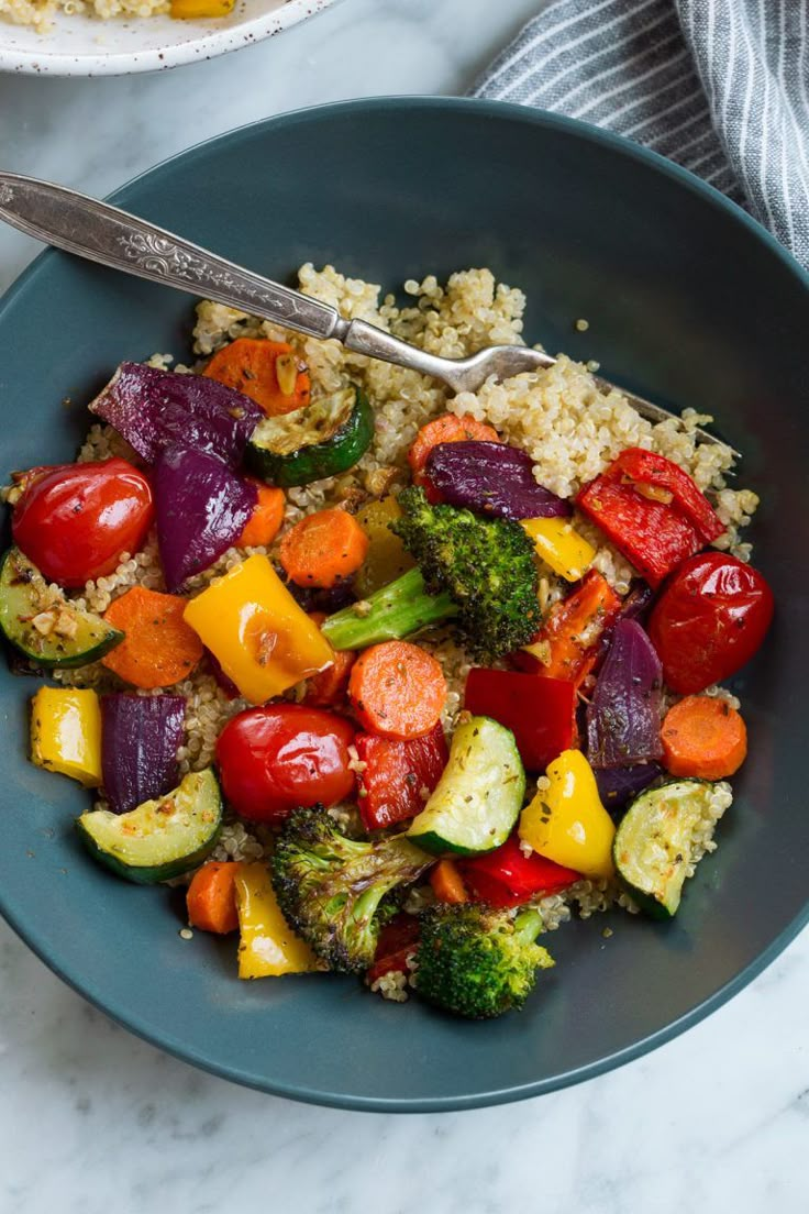 a bowl filled with vegetables and rice on top of a marble counter next to a fork