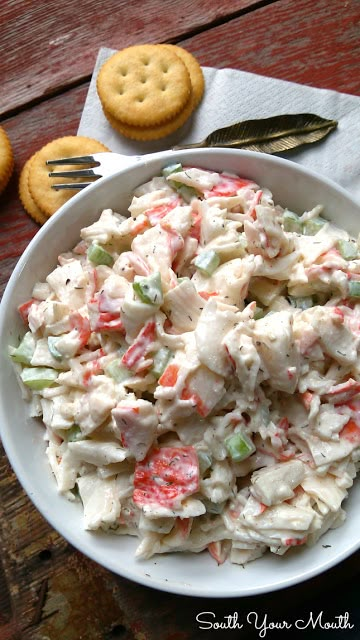 a white bowl filled with chicken salad next to crackers and a fork on a wooden table