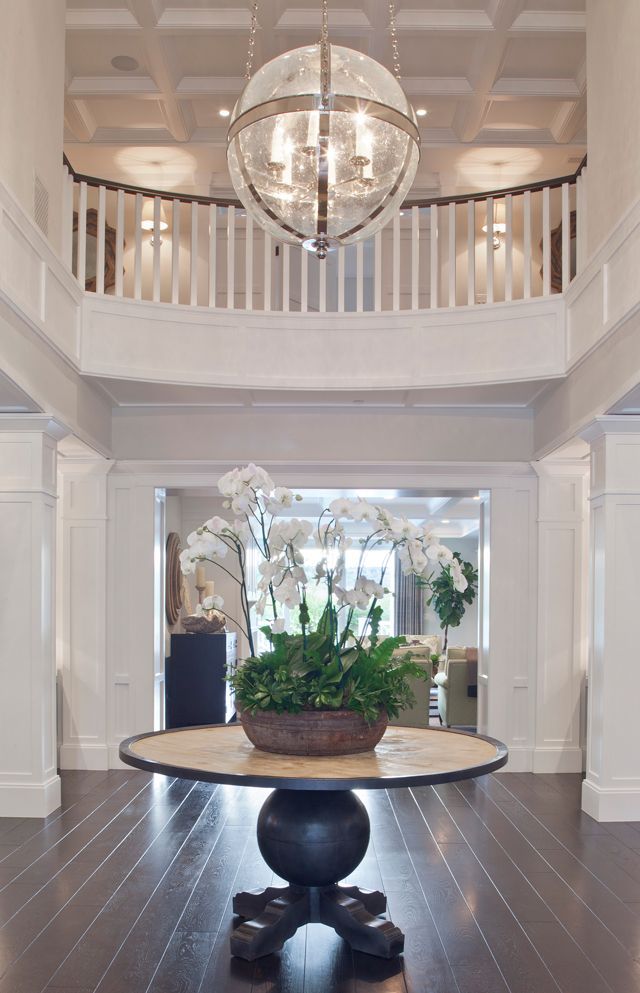 a large foyer with a chandelier and potted plants on the table in front of it