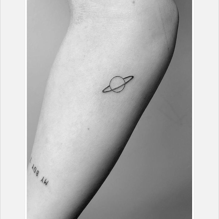 a small saturn tattoo on the left inner arm, with words written in cursive writing