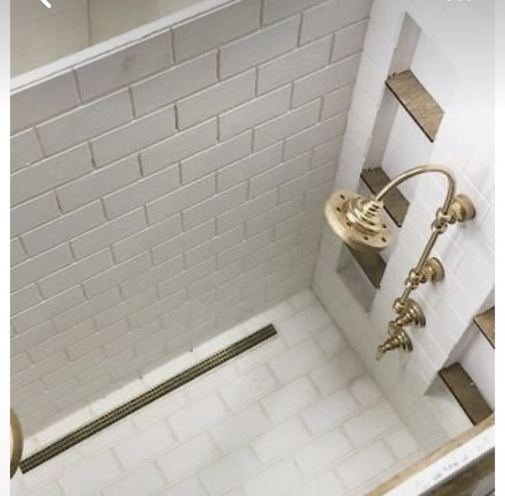 a white tiled shower with gold fixtures and no curtain in the bathtub is shown