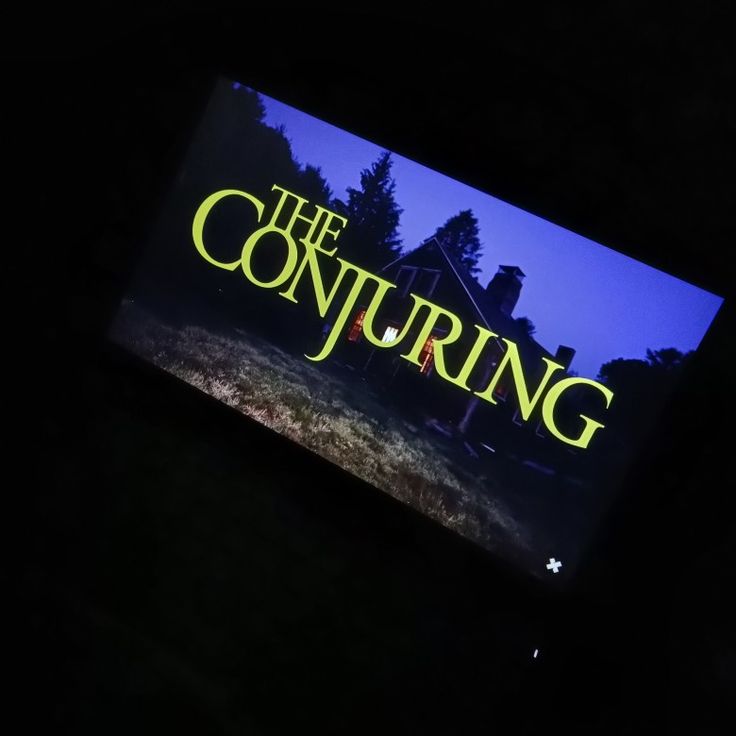 the conjuring title screen is lit up in the dark, with an image of a house behind it