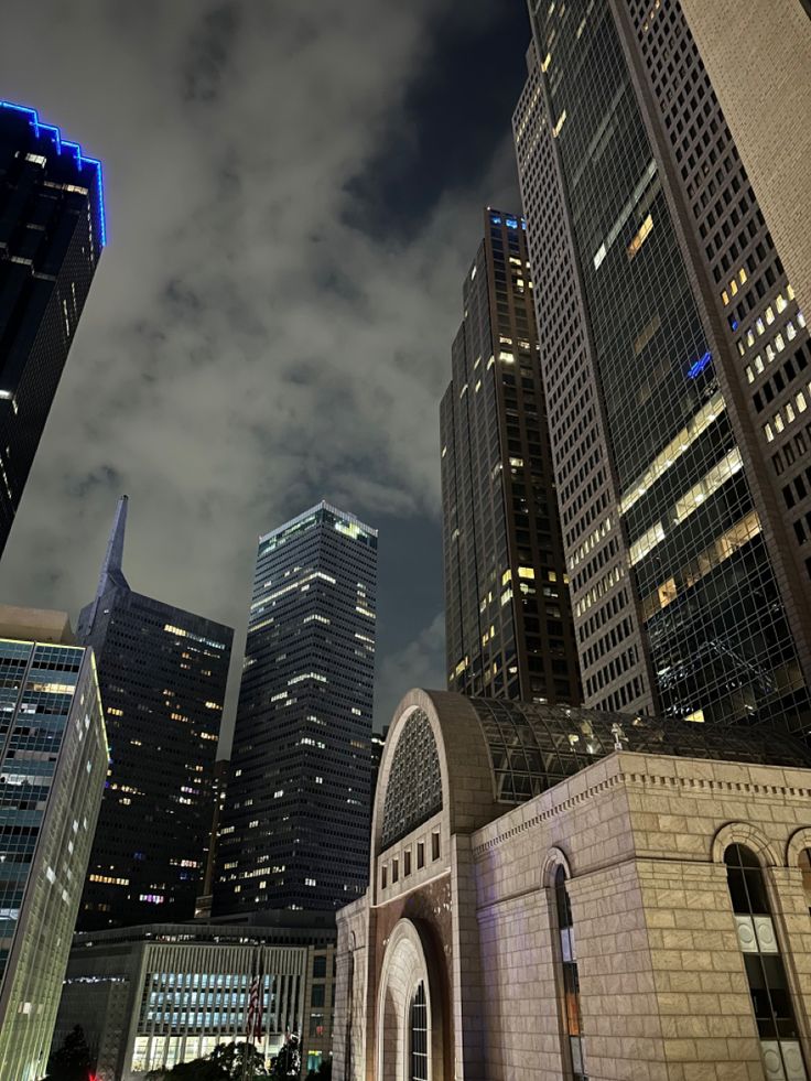 the city skyline is lit up at night with skyscrapers in the foreground and clouds in the background