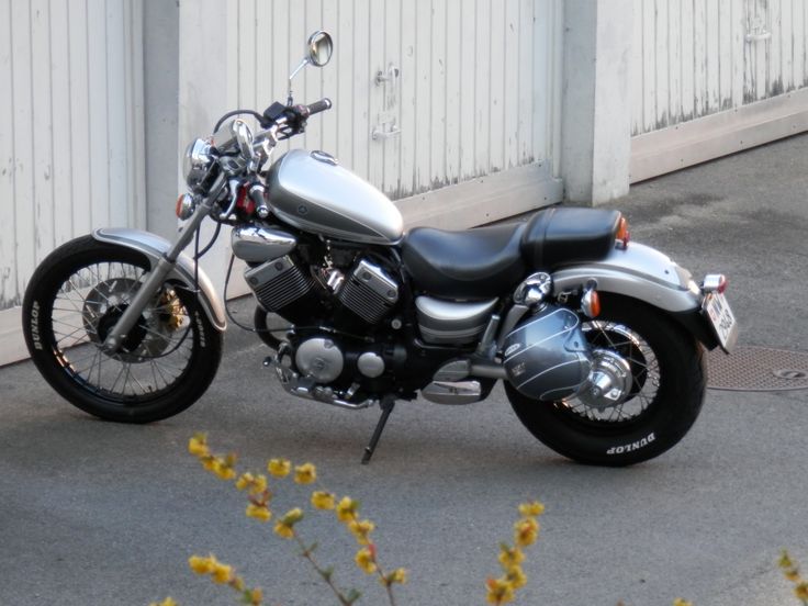 a motorcycle parked in front of a white building with yellow flowers on the ground next to it