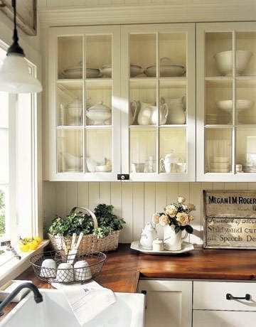 a kitchen with white cupboards filled with dishes and flowers on top of it's counter