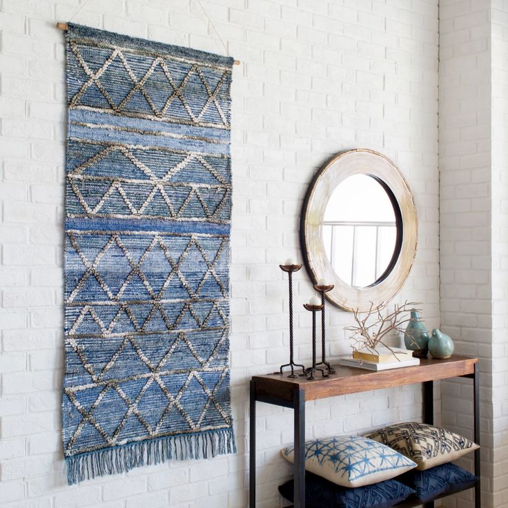 a white brick wall with a blue rug hanging on the wall and a mirror above it