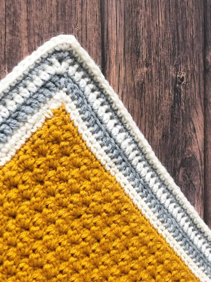 a crocheted yellow and gray rug on top of a wooden floor