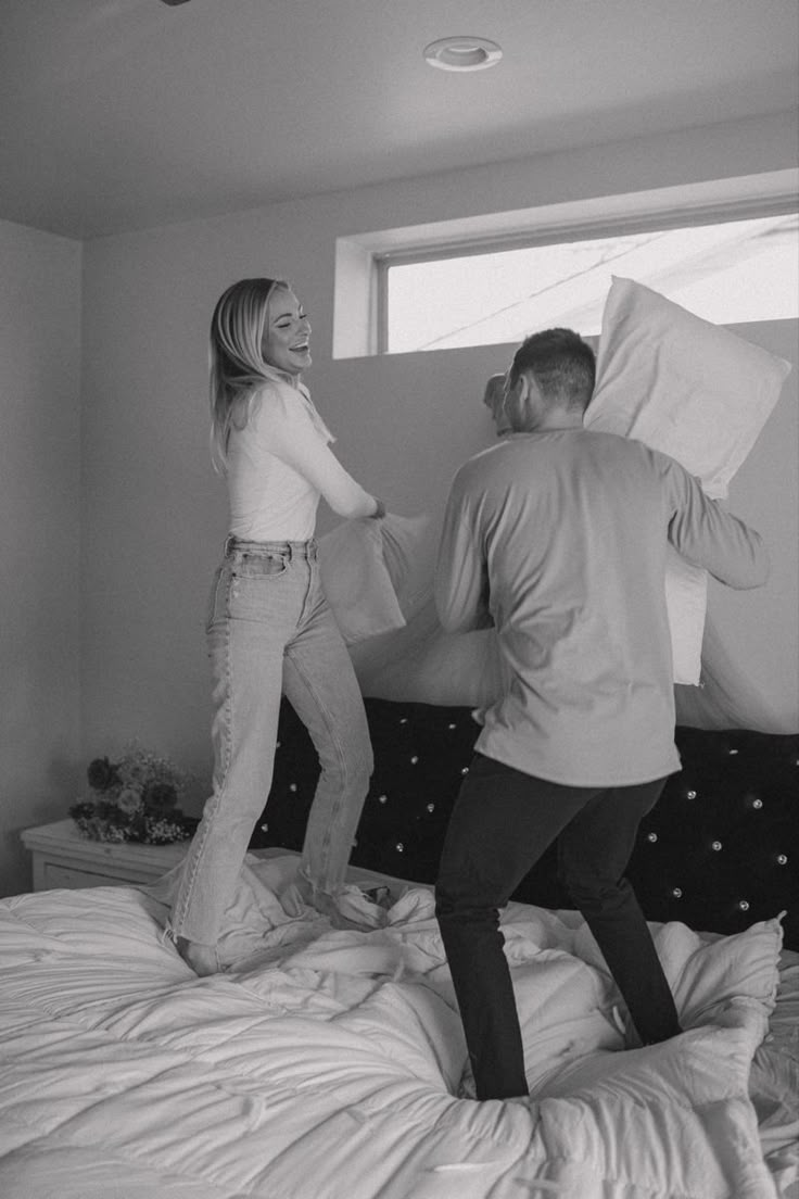 a man and woman standing on top of a bed next to each other with pillows