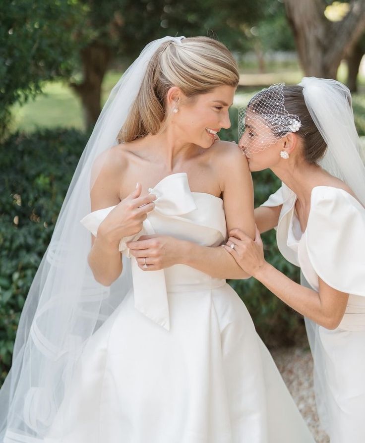 two beautiful women in wedding dresses standing next to each other with veils over their heads