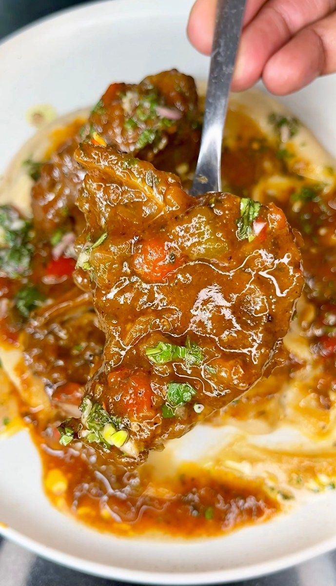 a person is holding a spoon over some food on a white plate with sauce and broccoli