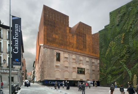 people are walking on the sidewalk in front of a building that has a vertical green wall