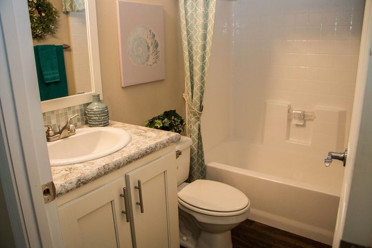 a white toilet sitting next to a bath tub under a bathroom mirror above a sink