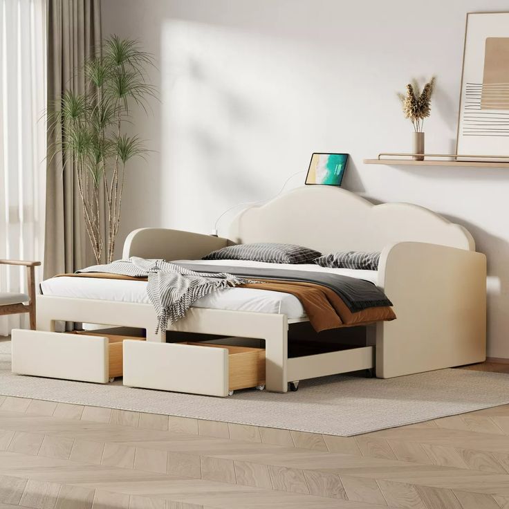 a white bed with drawers underneath it in a room next to a window and wooden flooring