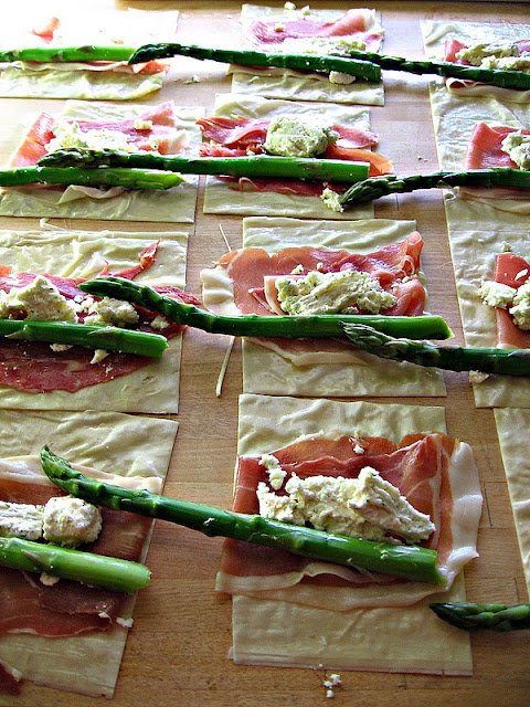 asparagus and prosciutto wrapped in paper on a cutting board with other food items