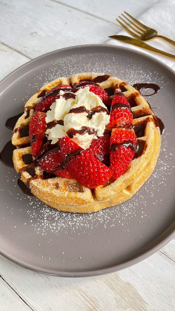 a waffle topped with strawberries and chocolate sauce on a plate next to a fork