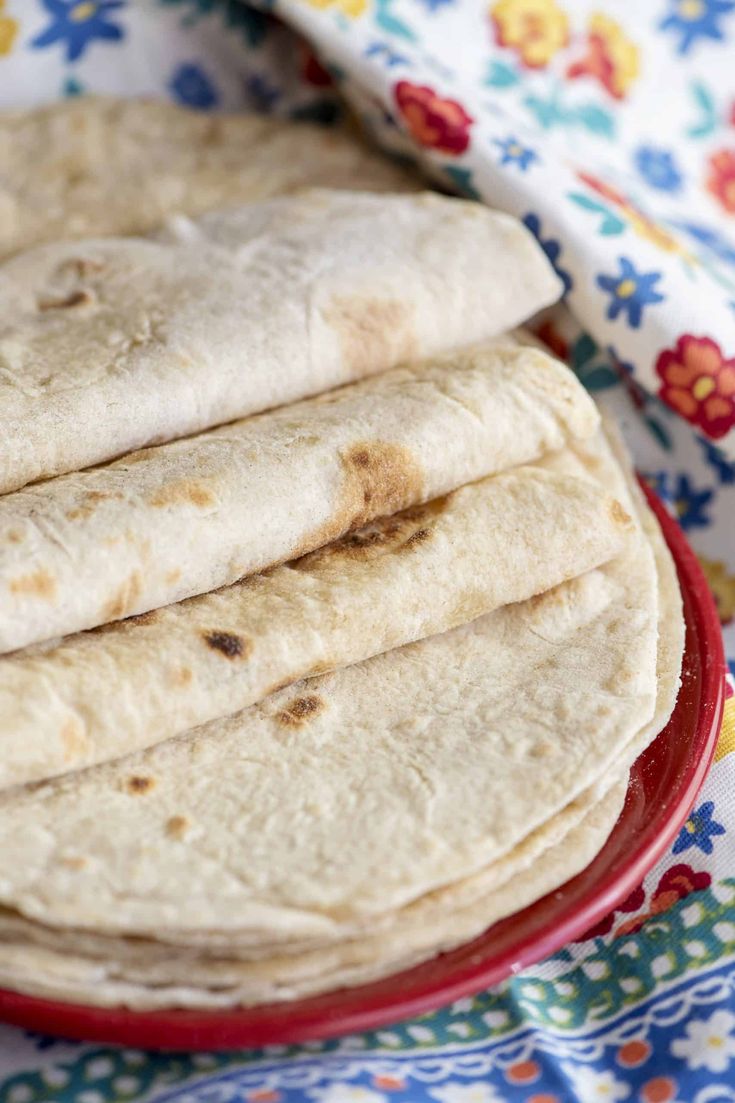 three tortillas on a red plate with a colorful flowered cloth behind it