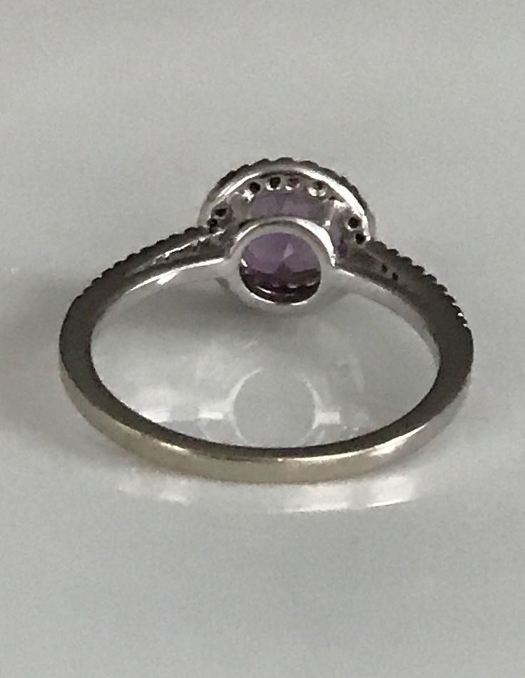 a white gold ring with an amethorate stone in the center, on a plain surface