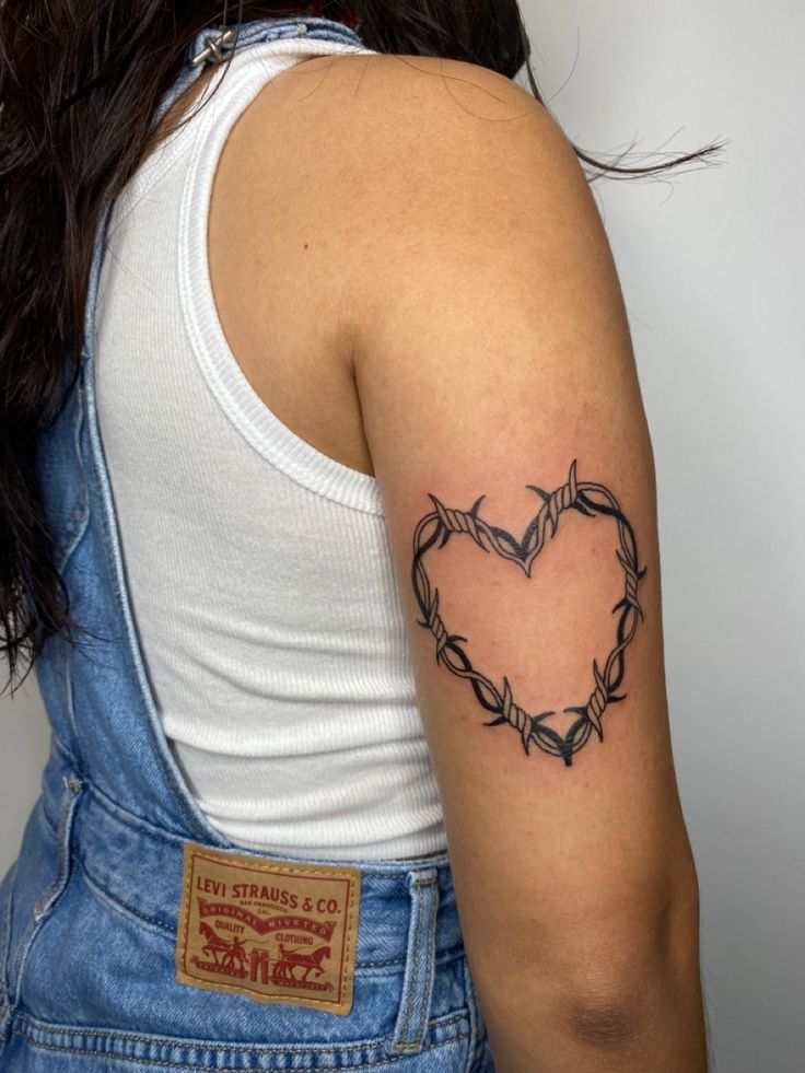 a woman with a tattoo on her arm and heart shaped barbed wire behind her back