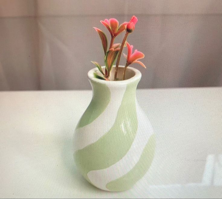 a green and white vase with pink flowers in it on a counter top next to a wall