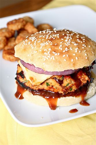 a chicken sandwich with sauce and onion on a plate next to some fried food items