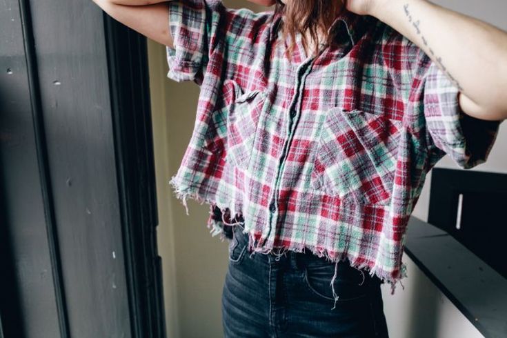 a woman with long hair wearing a red and green plaid shirt standing in front of a window