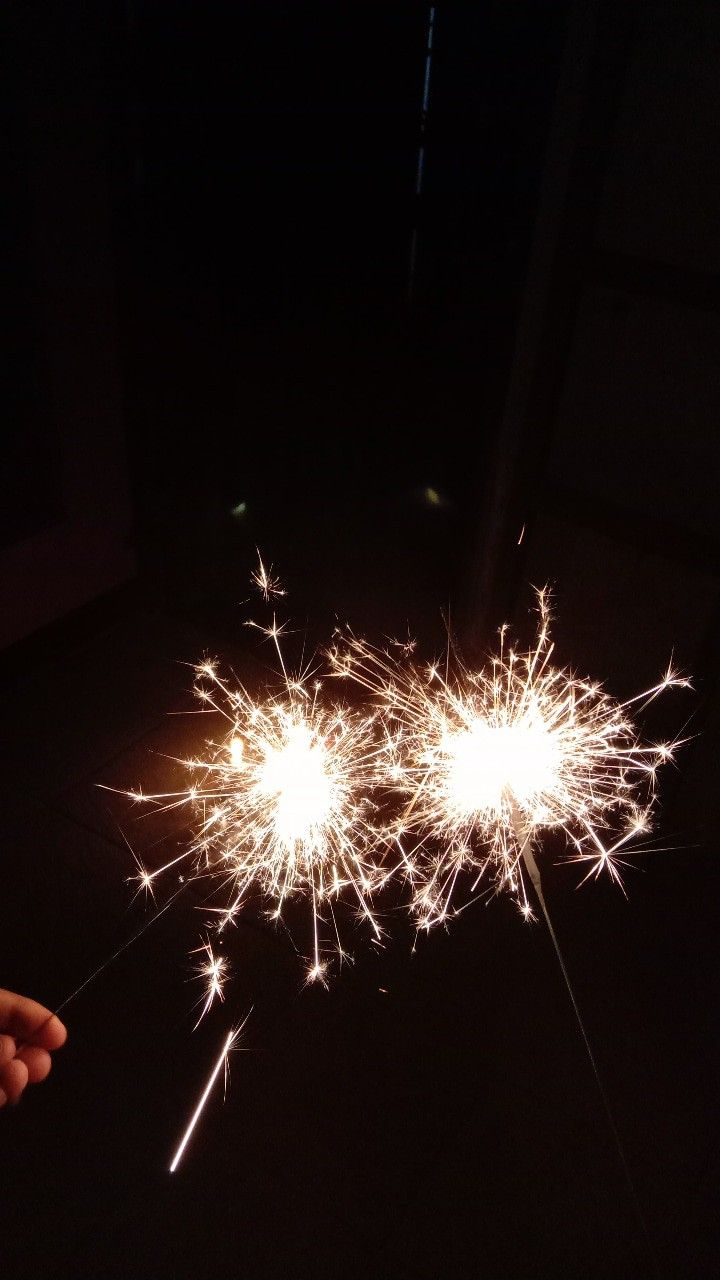 two sparklers in the dark with one being held up by someone's hand