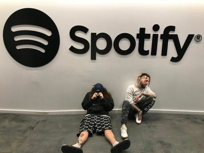 two people sitting on the ground in front of a spotify sign