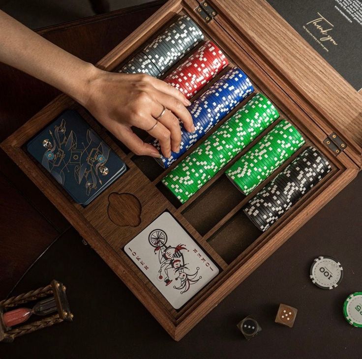 a person is playing cards in a wooden box with dices and other items on the table