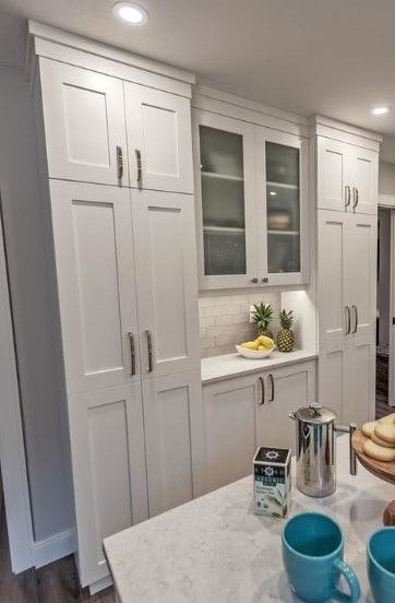 a kitchen with white cabinets and blue mugs on the counter top in front of it